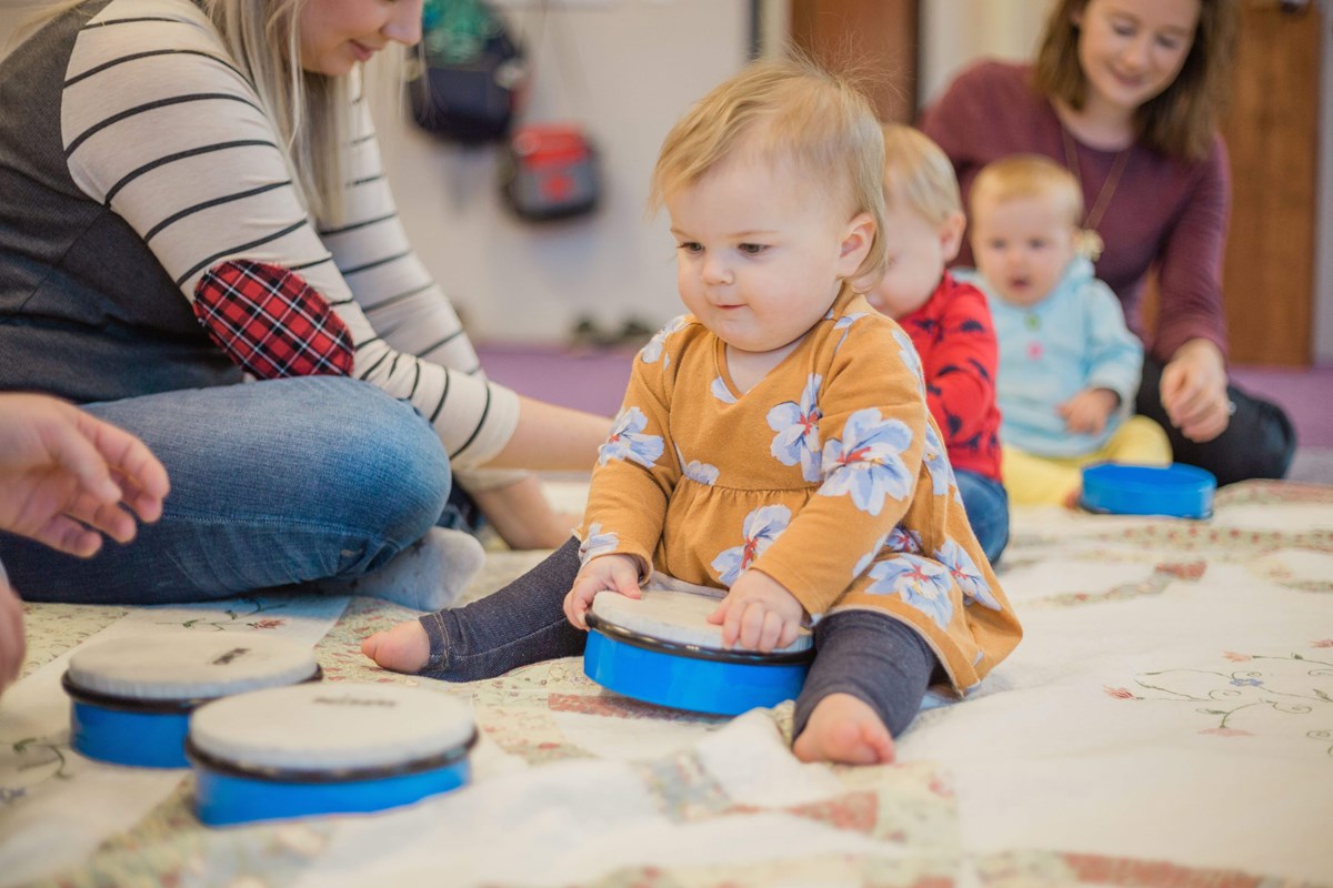 An 8-month-old girl grasps a drum during one of Kindermusik’s baby music classes.