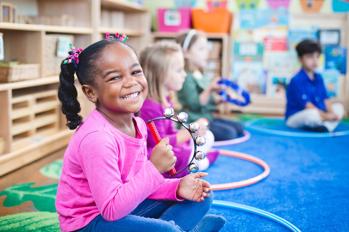 Girl playing tambourine. Kindermusik’s curriculum is based on various pieces of music and movement research.