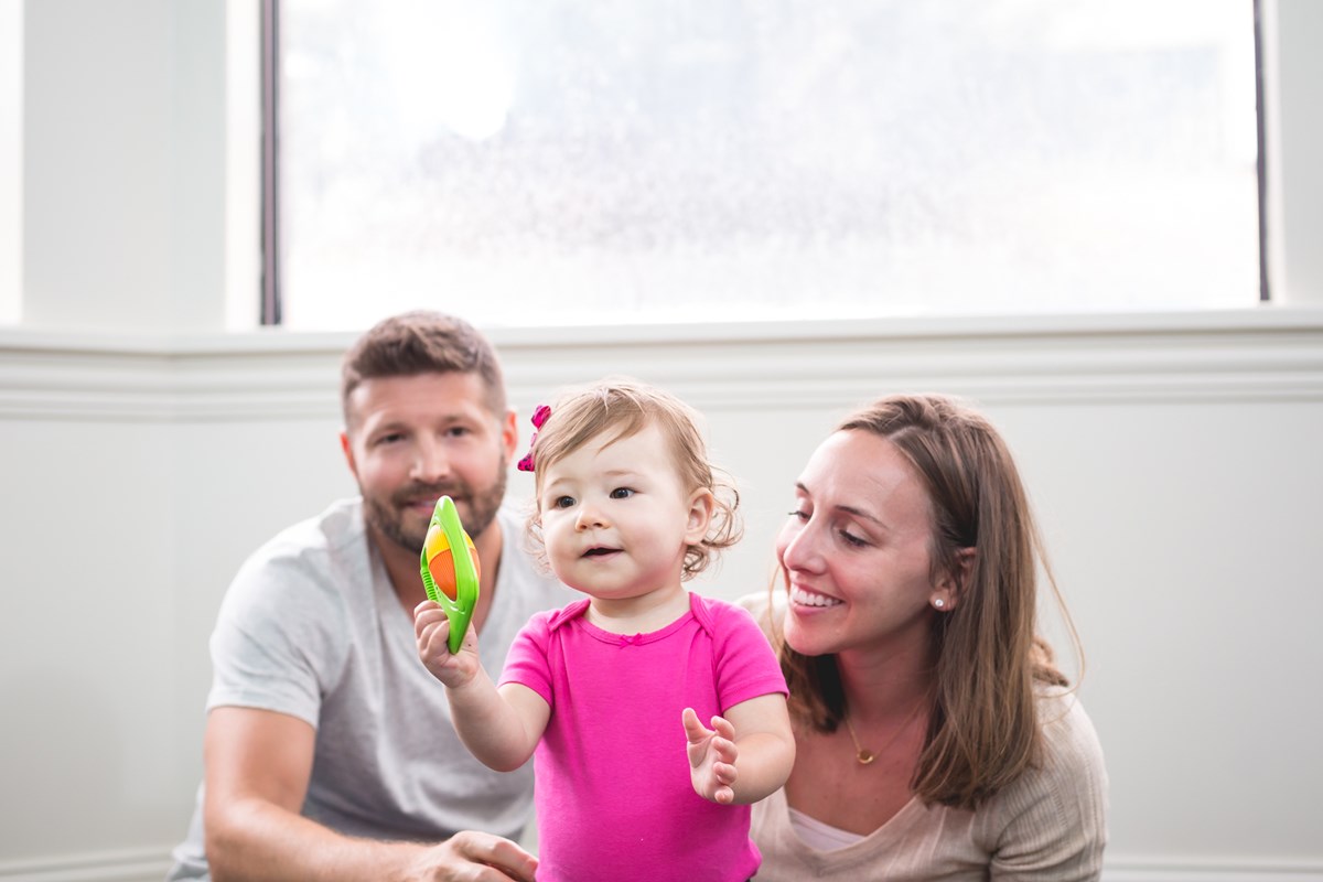 Mom, dad, and 2-year-old daughter playing with a shaker from Kindermusik’s Level 1 music programs for schools kit.