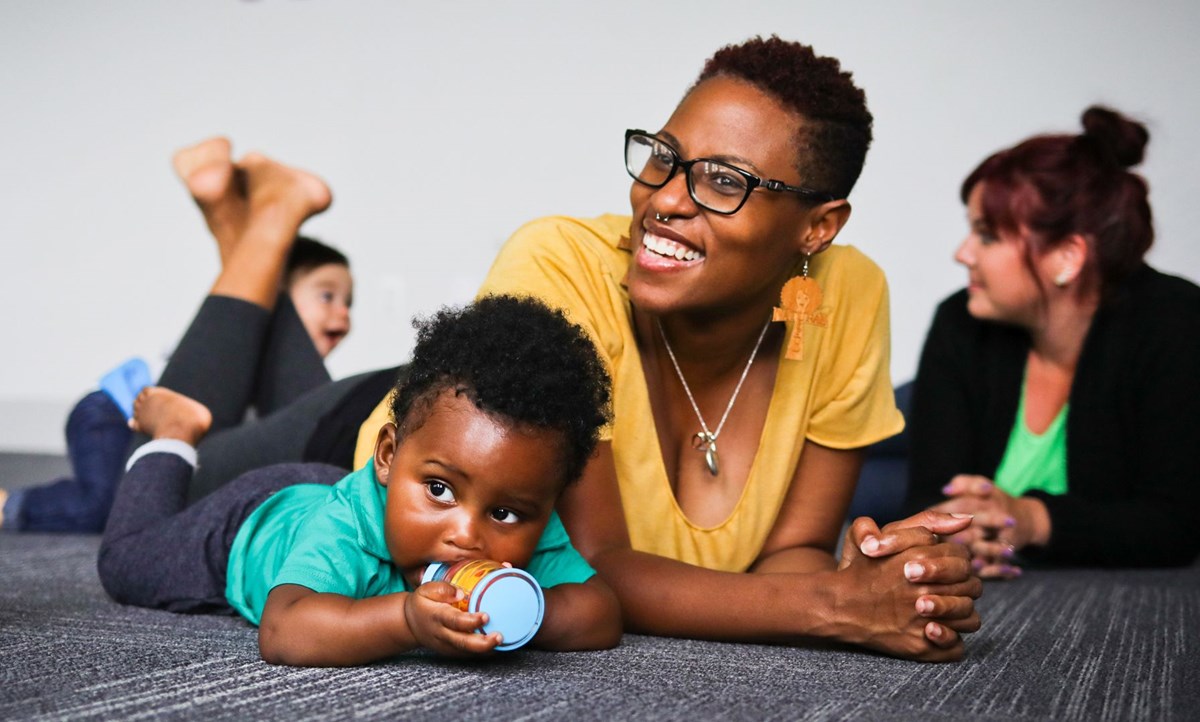 A mom and one-year old boy lay on the floor and explore shakers during one of Kindermsuik’s baby music classes.