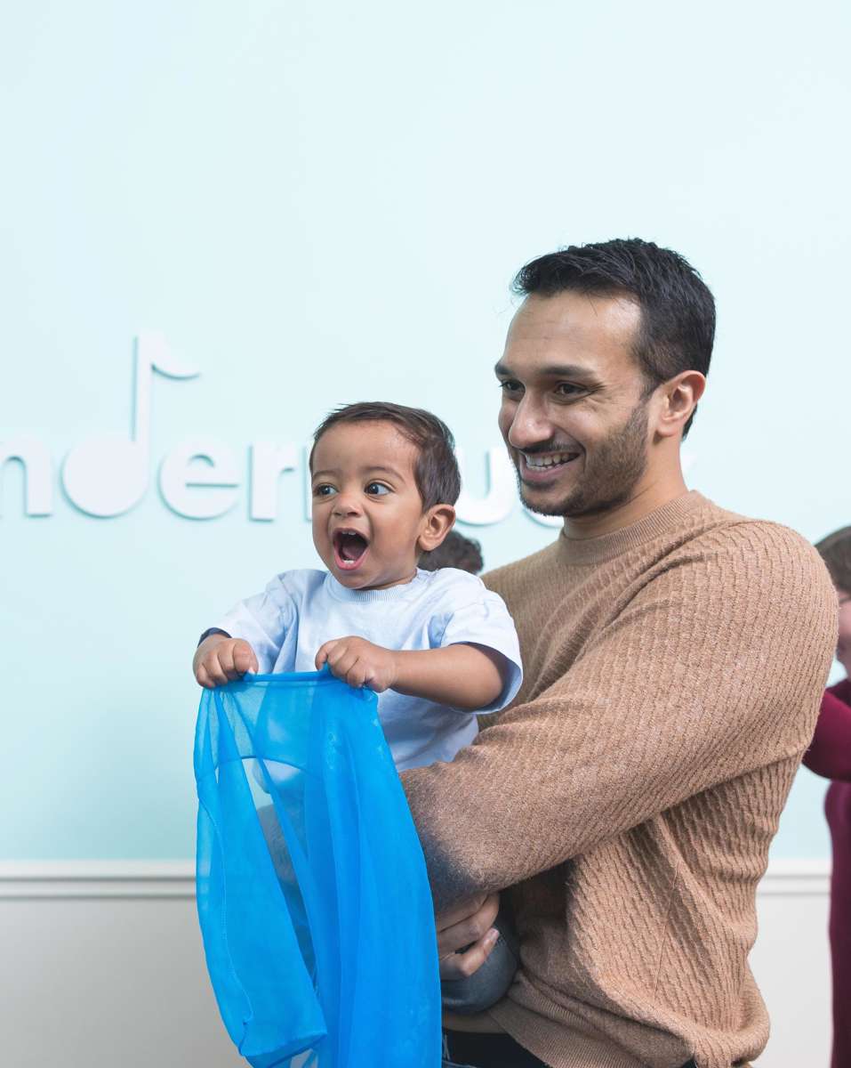 2-year-old boy waves a blue scarf with his dad during a Kindermusik class.